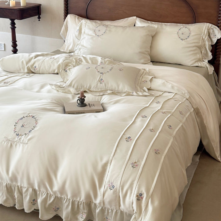 Satin bedding set with embroidered wreath motif, ruffled hem and decorative piping
