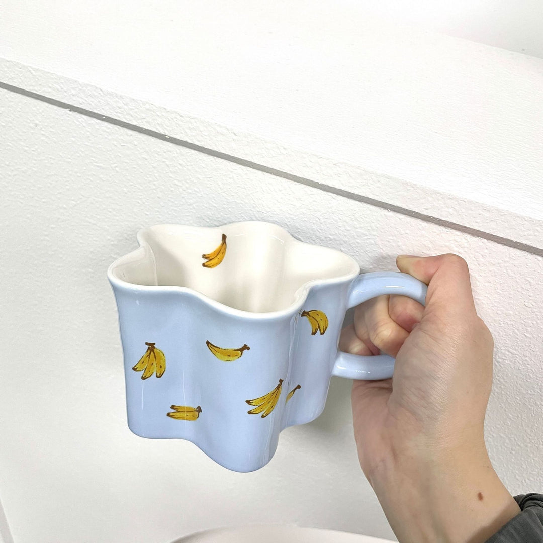 Ceramic coffee mug with flower-shaped wavy rim, illustrative banana decor and ergonomic handle