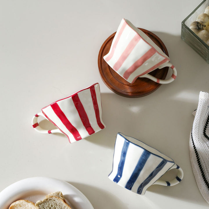 Sculptural ceramic coffee cup with curved rim and distinctive stripe decor