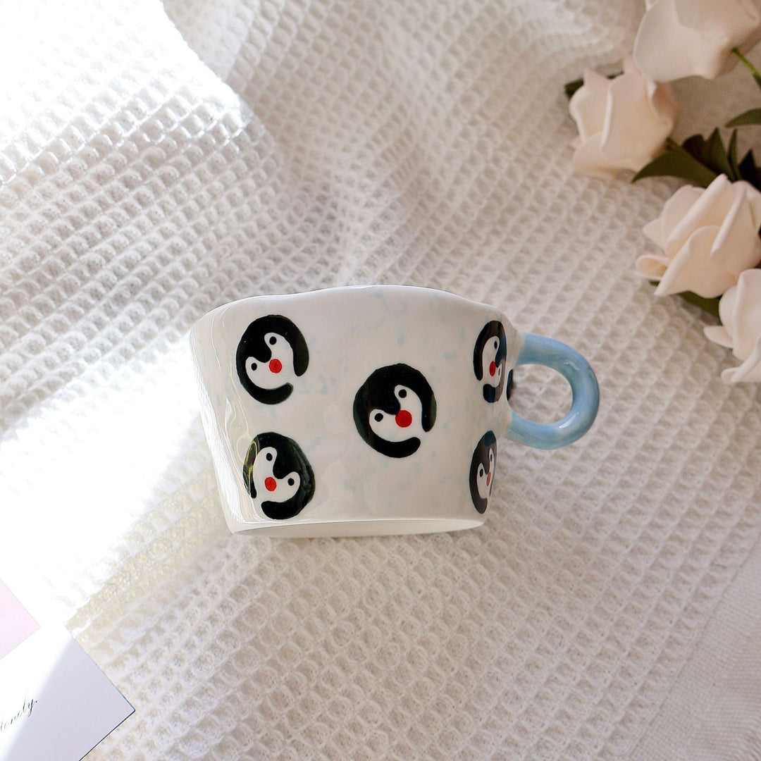 Ceramic coffee mug with hand-painted penguin designs and ergonomic handle