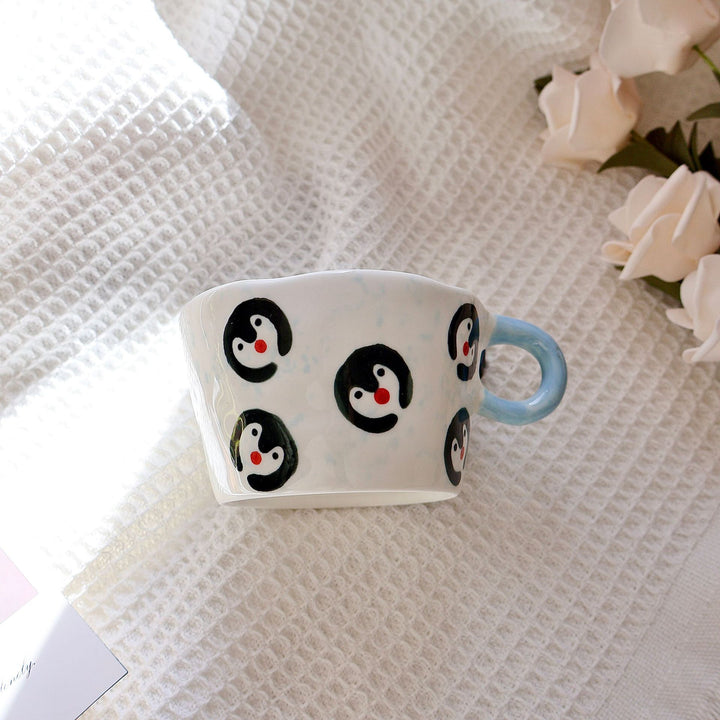 Ceramic coffee mug with hand-painted penguin designs and ergonomic handle
