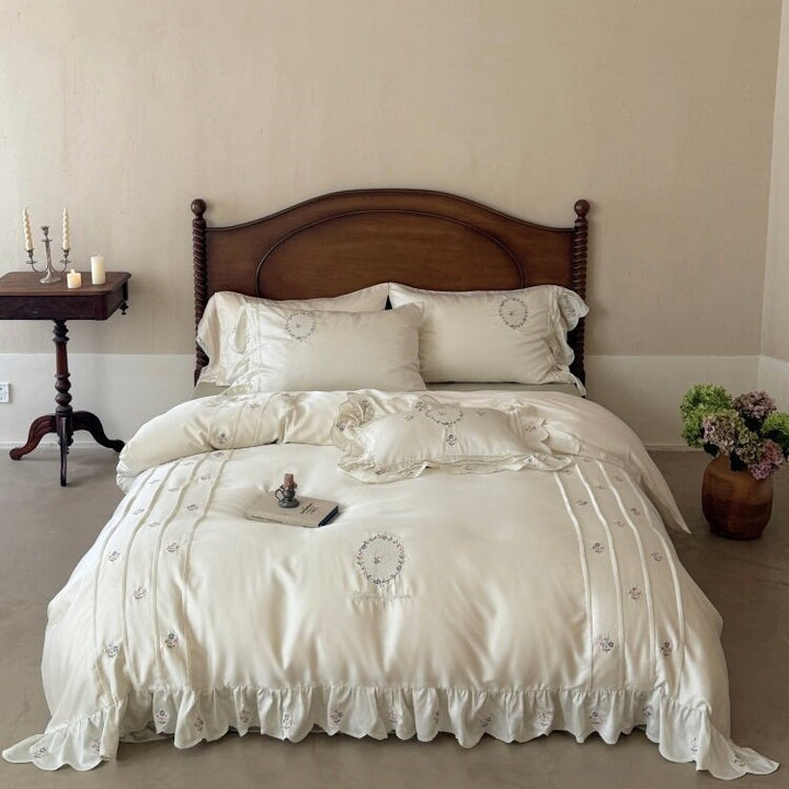 Satin bedding set with embroidered wreath motif, ruffled hem and decorative piping