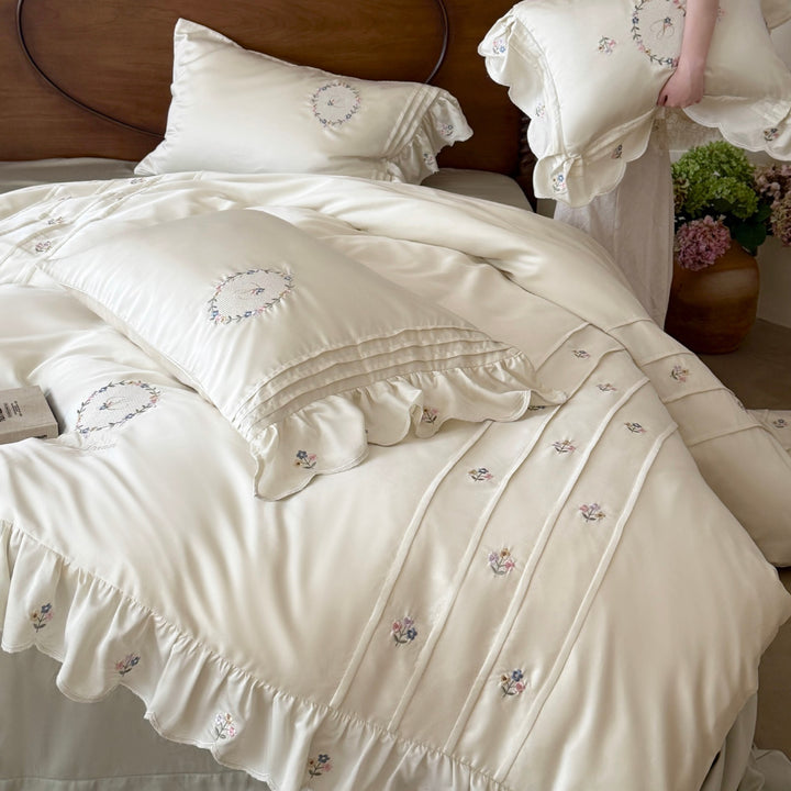Satin bedding set with embroidered wreath motif, ruffled hem and decorative piping