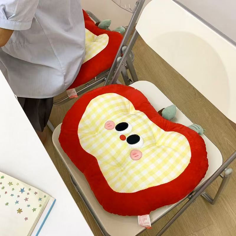 Padded children's seat cushion in apple shape with ergonomic seat recess and plush pendant