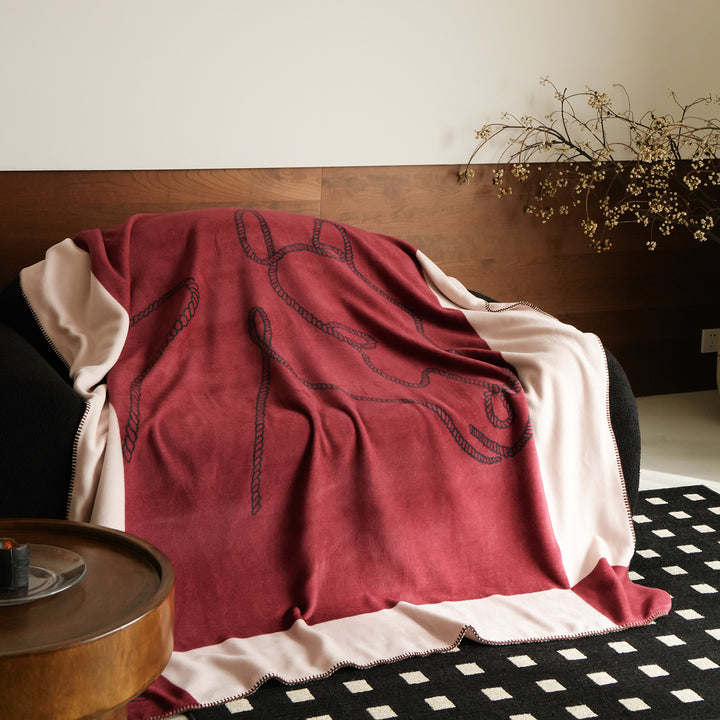 Throw blanket with embroidered cord motif and decorative stitching
